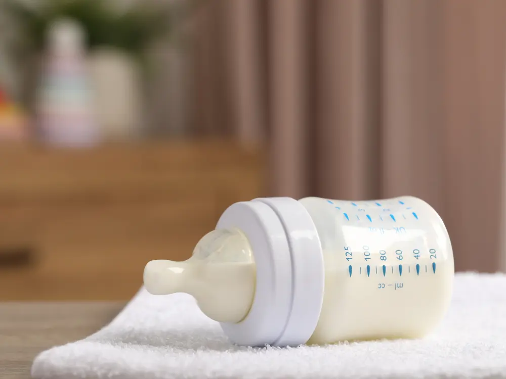 A baby bottle filled with formula resting on a white towel.